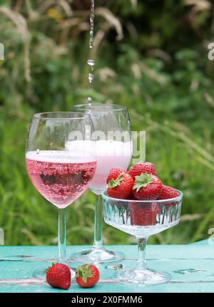 Zwei Gläser Rosenschaum und Erdbeere auf einem Tisch. Romantisches Picknick im Freien. Nahaufnahme des Glasgeschirrs. Getränke und Speisen im Sommer. Stockfoto