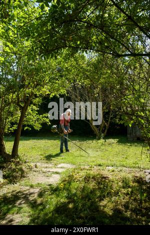 Ein älterer Mann, der mit einer Freischneide Gras in seinem ländlichen Garten in zala, ungarn, abschneidet Stockfoto