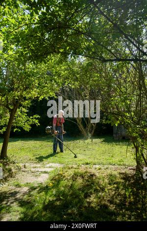 Ein älterer Mann, der mit einer Freischneide Gras in seinem ländlichen Garten in zala, ungarn, abschneidet Stockfoto