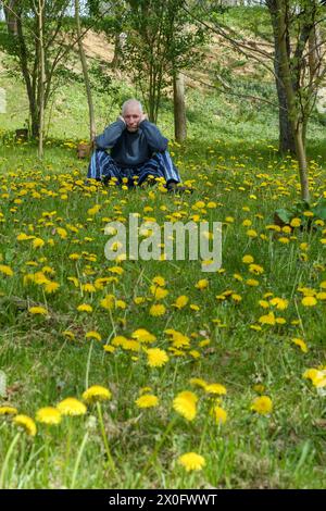 Ein älterer Mann, der schmutzig und niedergeschlagen aussah, saß im Garten, umgeben von Löwenzahn taraxacum, der seinen ländlichen Garten in zala, ungarn, eroberte Stockfoto