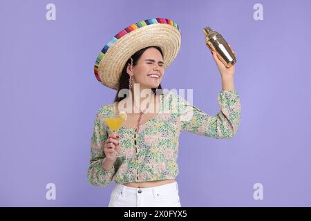 Junge Frau in mexikanischem Sombrero-Hut mit Cocktail und Shaker auf violettem Hintergrund Stockfoto