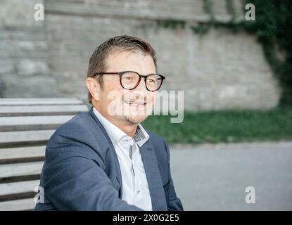 Ein nachdenklicher Geschäftsmann im Anzug sitzt auf der Bank in urbaner Umgebung Stockfoto