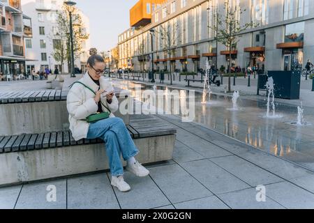 Frau in Jeans und Jacke in der Stadt mit Handy Stockfoto