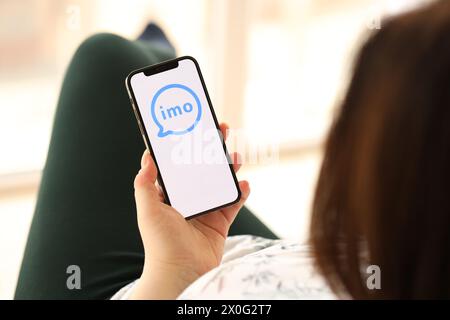 KIEW, UKRAINE - 1. APRIL 2024 IMO-Messenger-Symbol auf dem Smartphone-Bildschirm in jungen weiblichen Händen drinnen. Frau, die zu Hause die iPhone App nutzt Stockfoto