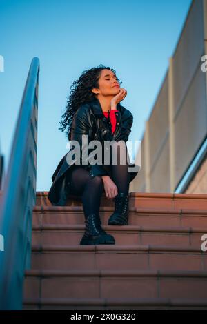 Frau mit lockigen Haaren, die auf Stufen des Gebäudes sitzt Stockfoto