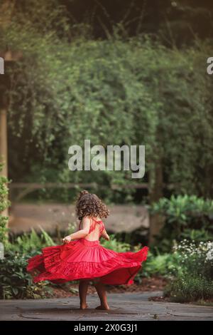 Mädchen in Rot wirbelt fröhlich auf einem Gartenweg Stockfoto