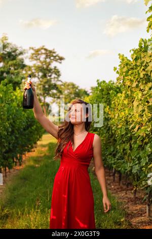 Eine junge italienerin, die auf eine Prosecco-Flasche blickt, während sie in einem Weinberg ist Stockfoto