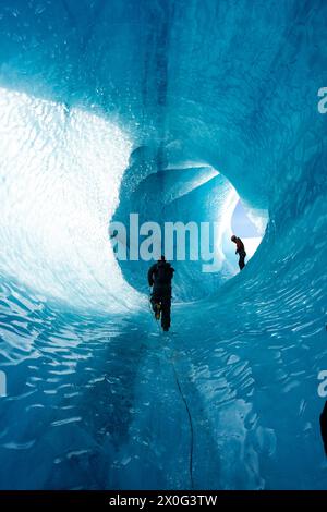 Mann klettert auf die Gletscherhöhle in Island - Winter Gear - Blauer Eisberg Stockfoto