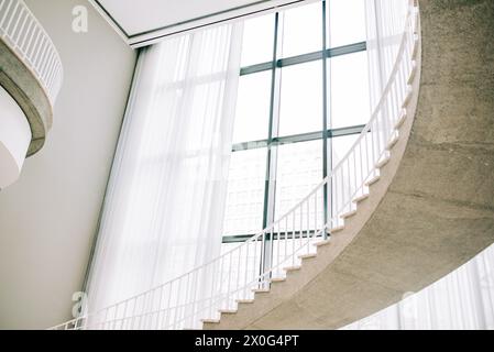 Atemberaubende Wendeltreppe in Licht getaucht von einem hoch aufragenden Fenster Stockfoto