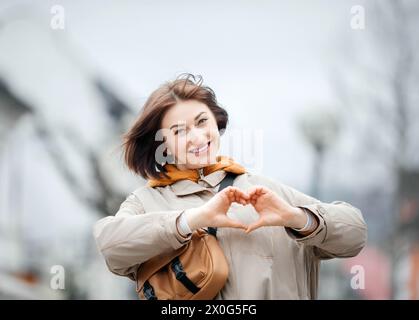 Charmante Frau, die Herzform mit Händen auf urbanem Hintergrund macht Stockfoto
