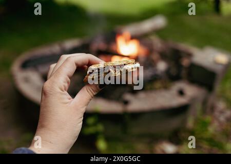 Nahaufnahme einer Hand, die frisch gemachtes s'more über dem Hinterhof-Feuer hält Stockfoto