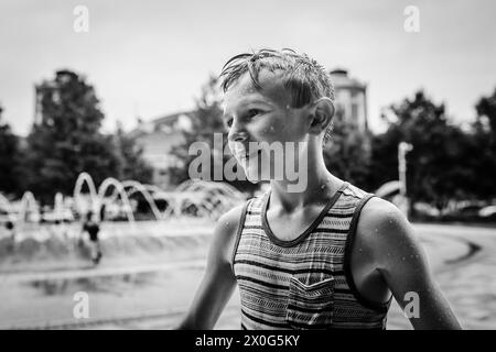 Kind im Sommer mit Wassertropfen am Stadtbrunnen bedeckt Stockfoto