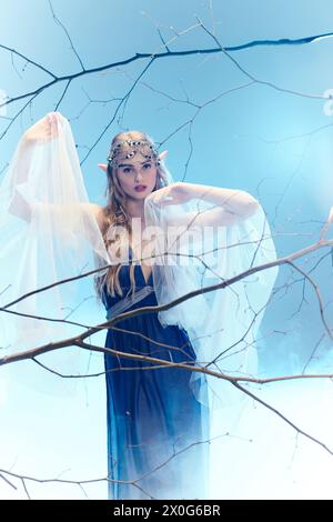 Eine junge Frau strahlt märchenhafte Magie in einem blauen Kleid und weißem Schleier in einer skurrilen Atelierumgebung aus. Stockfoto