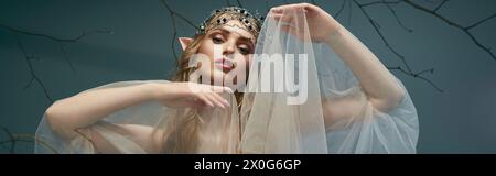 Eine junge Frau mit Diadem und Schleier posiert anmutig vor einem majestätischen Baum und verkörpert den Geist einer Elfenprinzessin. Stockfoto