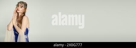 Eine junge Frau, die einer ätherischen Elfenprinzessin ähnelt, posiert elegant in einem blau-weißen Kleid in einem Studio-Setting. Stockfoto