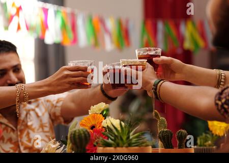 Hände von vier jungen Leuten, die mit Tequila-Gläsern über festlichem Tisch mit Gerberas und Kakteen auf der Party toasten Stockfoto