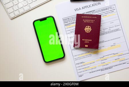Draufsicht eines Visumantrags mit deutschem Reisepass und einem Smartphone mit grünem Bildschirm auf dem Tisch Stockfoto
