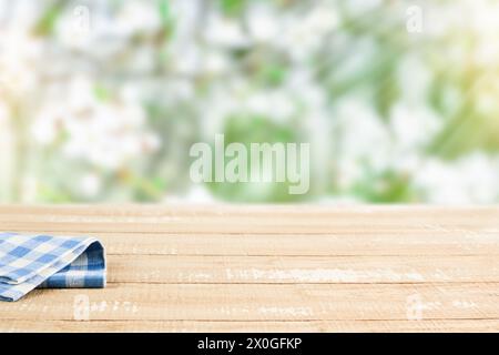 Leerer rustikaler Holztisch mit blauer Tischdecke über blühendem Sommergarten auf sonnigem Tageshintergrund. Ernten Sie Mock-up für Design. Stockfoto