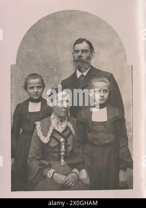 Familienporträt: Eltern und zwei Zwillingsmädchen (10-12 Jahre) Eltern im Zentrum umgeben von den stehenden Kindern. Alles in festlichen Kostümen. Damenkleid mit Tüllärmeln, breitem Kragen mit weißem Besatz, Vater mit Gehrock und Vollbart, alle sehen sehr ernst aus, Mutter und Vater haben einen älteren, getragenen Ausdruck, Mädchen mit demselben Kleid mit angenähtem Schulterkragen und weißem Blusenaufsatz [automatisierte Übersetzung] Stockfoto