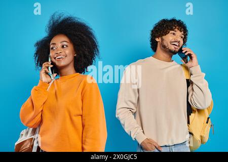 Ein Mann und eine Frau, interrassische Studenten, stehen zusammen in lässiger Kleidung, unterhalten sich auf Handys. Blauer Hintergrund im Studio. Stockfoto