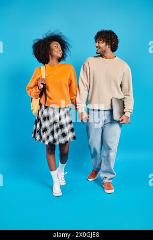 Ein zwanglos gekleidetes Paar macht einen gemütlichen Spaziergang vor einem leuchtend blauen Hintergrund in einem Studio. Stockfoto