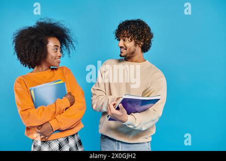 Zwei interrassische Studenten stehen nebeneinander vor blauem Hintergrund und symbolisieren Einheit und Vielfalt. Stockfoto