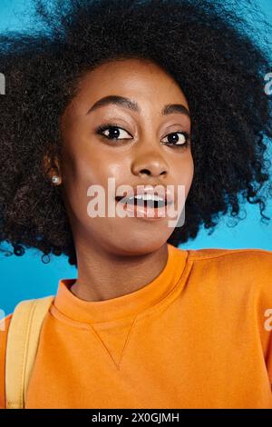 Ein afroamerikanischer Student mit einem voluminösen Afro, der sich selbstbewusst vor blauem Hintergrund in einem Studio posiert. Stockfoto