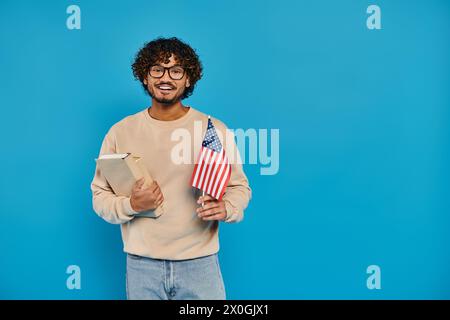 Ein Mann hält stolz ein Buch und eine amerikanische Flagge, die vor blauem Hintergrund in einem Studio steht. Stockfoto