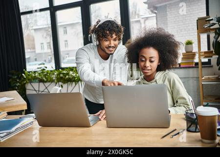 Ein Mann und eine Frau, die in ihre Arbeit eingetaucht sind, konzentrieren sich leidenschaftlich auf einen Laptop-Bildschirm in einem modernen Coworking-Raum. Stockfoto