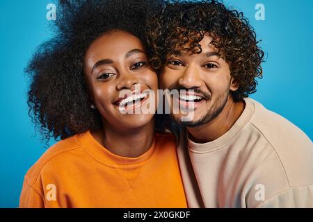 Ein Mann und eine Frau, die interrassische Harmonie repräsentieren, lächeln hell in einem Studio mit blauem Hintergrund. Stockfoto