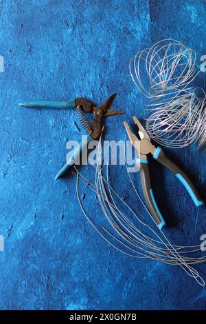 Vintage-Zange, Draht und Armierungsstahl auf blauem strukturiertem Hintergrund mit Kopierbereich. Renovierungsarbeiten im Detail. Stockfoto