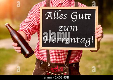 12. April 2024: Happy Men's Day Greeting auf einem Brett, das von einem Mann in Lederhosen zusammen mit einer Flasche Bier gehalten wird. Gruß zum Männentag. PHOTOMONTAGE *** alles Gute zum Herrentag Gruß auf einer Tafel die ein Mann in Lederhose zusammen mit einer Flasche Bier hält. Herrentagsgruß. FOTOMONTAGE Stockfoto