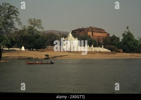 Ein Boot passiert den unfertigen Mingun Pahtodawgyi Stupa hinter einer weißen Pagode in Mingun, etwa elf Kilometer flussaufwärts von Mandalay. [Automatisierte Übersetzung] Stockfoto