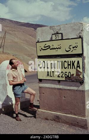 Ein Tourist steht vor einem Straßenschild am 2260 m hohen Tichka-Pass (Col du Tichka) im Atlas-Gebirge. [Automatisierte Übersetzung] Stockfoto