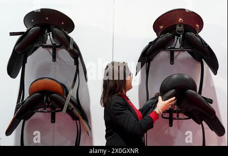 Schleswig-Holstein, Neumünster, Deutschland. 12. April 2024. Ein Mitarbeiter hängt einen Reitsattel an der Wand des Iberosattel-Standes auf der Nordpferd-Messe in den Holstenhallen. Die Messe für Pferde und Reitsport findet vom 12. Bis 14. April statt. Foto: Marcus Brandt/dpa/Alamy Live News Stockfoto