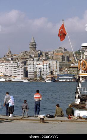 Eine Familie sitzt und setzt am Pier am Goldenen Horn in Istanbul. Einer der Männer ist der Fischfang. Im Hintergrund der Galata-Turm. [Automatisierte Übersetzung] Stockfoto