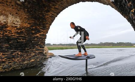 Tragflächenreiter gleitet mit seinem Brett in einem der Kanäle der Ria de Aveiro in Portugal während des Sonnenuntergangs über dem Wasser. Stockfoto