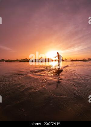 Tragflächenreiter gleitet mit seinem Brett in einem der Kanäle der Ria de Aveiro in Portugal während des Sonnenuntergangs über dem Wasser. Stockfoto