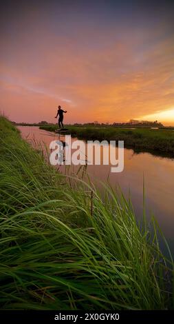 Tragflächenreiter gleitet mit seinem Brett in einem der Kanäle der Ria de Aveiro in Portugal während des Sonnenuntergangs über dem Wasser. Stockfoto