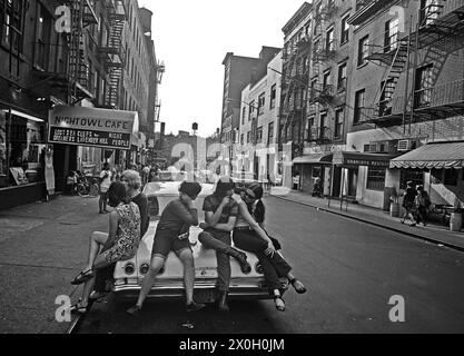 Eine Gruppe Jugendlicher sitzt auf der Motorhaube eines Autos vor einem Cafe in einer Straße im New Yorker Greenwich Village entfernt. Stockfoto