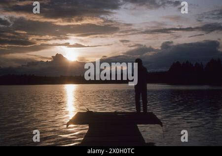 Ein Mann auf einem Steg in der Mitternachtssonne auf einem finnischen See. Stockfoto