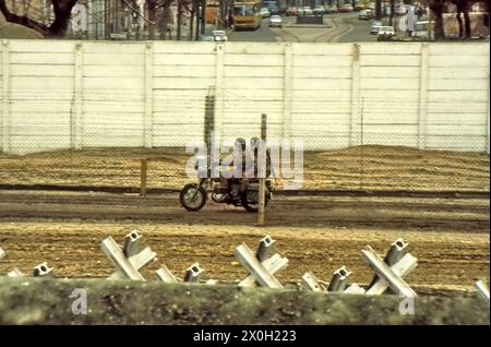 Soldaten der Nationalen Volksarmee (NVA) auf einer Motorradfahrt entlang der Grenze. Im Vordergrund befinden sich Panzerschranken und im Hintergrund eine Straße in Ost-Berlin. Stockfoto