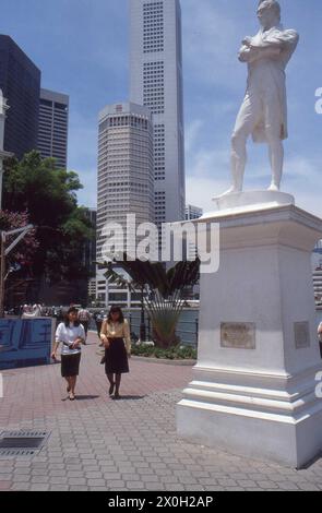 Die Statue von Sir Thomas Stamford Bingley Raffles in Singapur. Daneben gibt es Fußgänger und im Hintergrund Wolkenkratzer. Stockfoto