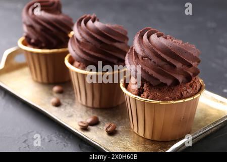Köstliche Schokoladen-Cupcakes und Kaffeebohnen auf schwarzem, strukturiertem Tisch, Nahaufnahme Stockfoto