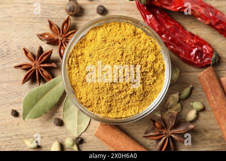 Currypulver in Schüssel und andere Gewürze auf Holztisch, flach gelegt Stockfoto