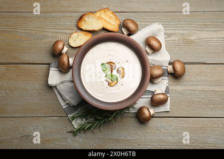 Leckere hausgemachte Pilzsuppe im Keramiktopf, Croutons, frische Champignons und Rosmarin auf Holztisch, flach gelegt Stockfoto