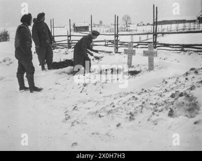 Drei Soldaten ehren ihre gefallenen Kameraden an der Ostfront, indem sie Tannenzweige auf ihre Gräber legen. Das Bild wurde von einem Mitglied des Radfahrgrenadierregiments 2/Radfahrsicherungsregiment 2 im Nordteil der Ostfront aufgenommen. [Automatisierte Übersetzung] Stockfoto