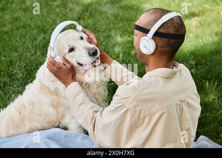 Ein vielseitiger Mann mit Myasthenia gravis-Syndrom sitzt auf Gras und streichelt freudig seinen treuen Labrador-Hund, während beide Kopfhörer tragen. Stockfoto