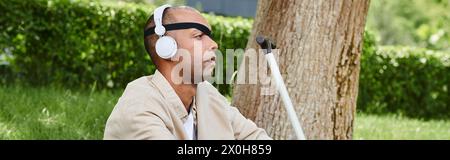 Ein Mann mit Kopfhörern genießt Musik neben einem Baum und zeigt Vielfalt und Inklusion. Stockfoto