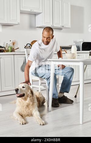 Ein behinderter Afroamerikaner sitzt mit seinem Labrador-Hund an einem Tisch, beide genießen einen friedlichen Moment zusammen. Stockfoto